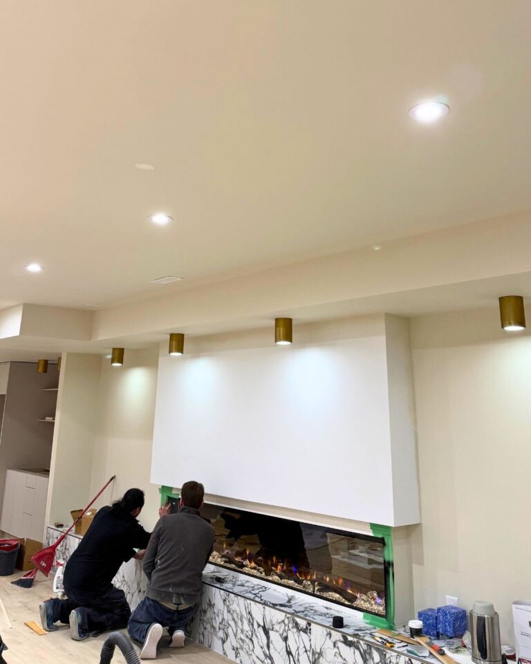 Finished living room with pot lights and wall sconces above a fireplace