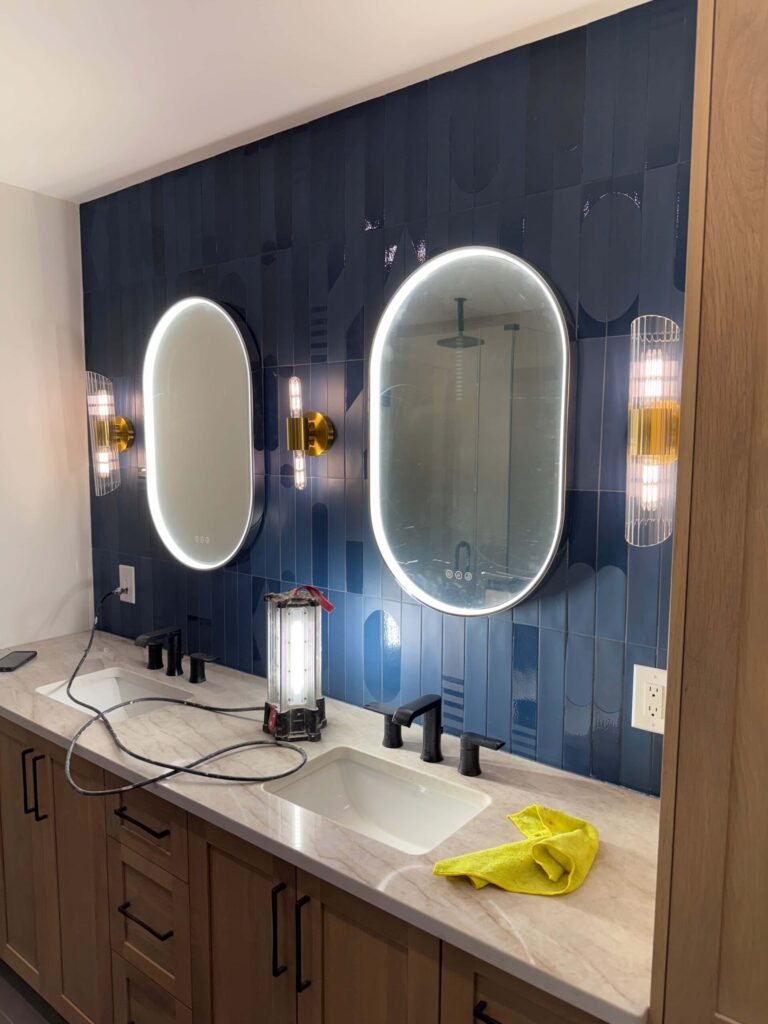 Bathroom vanity with backlit oval mirrors and wall sconces
